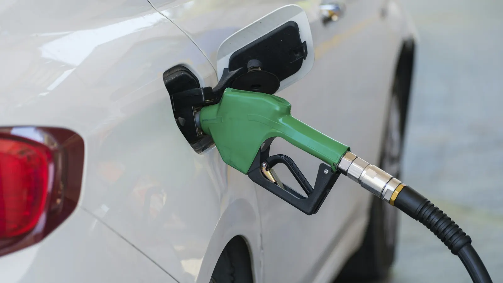 A green fuel nozzle in the open fuel door of a white car at a gas pump
