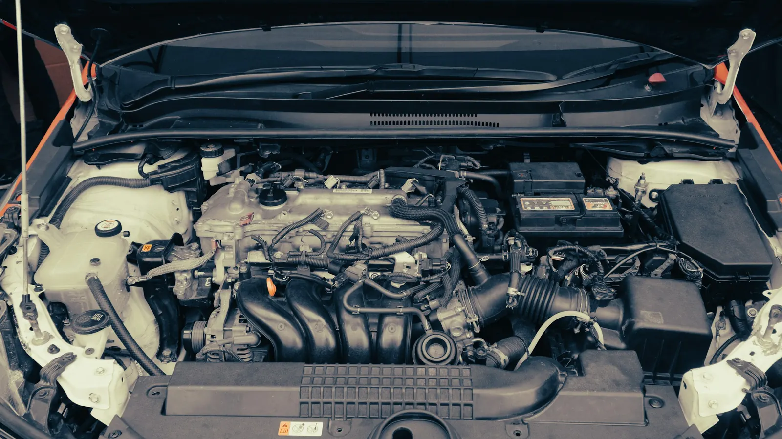 Open hood of a compact car showing the engine, with the 12-volt battery at the upper right