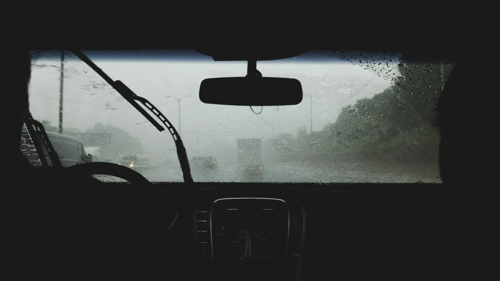 View from inside a car of a rain-soaked windshield and wipers on a wet highway